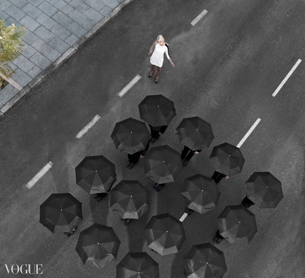 Aerial fashion photography - woman in white facing a formation of black umbrellas